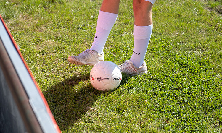 Eine Person steht auf dem Rasen und spielt gerade mit dem Ball, der vor den Beinen liegt Eine Person steht auf dem Rasen und spielt gerade mit dem Ball, der vor den Beinen liegt