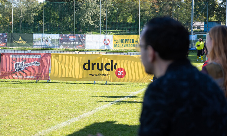 Eine Person blickt als Zuschauer auf den Fußballplatz, im Hintergrund ist ein druck.at Banner zu sehen Eine Person blickt als Zuschauer auf den Fußballplatz, im Hintergrund ist ein druck.at Banner zu sehen