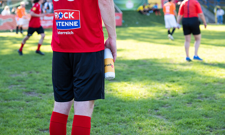 Ein Fußballspieler steht am Rasen und hält eine gebrandete Trinkflasche in der Hand Ein Fußballspieler steht am Rasen und hält eine gebrandete Trinkflasche in der Hand