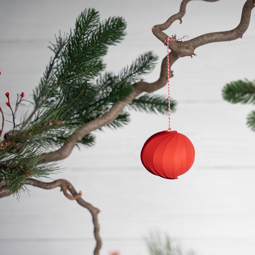 Selbst gebastelte Weihnachtskugel aus rotem Papier hängt auf einem Ast