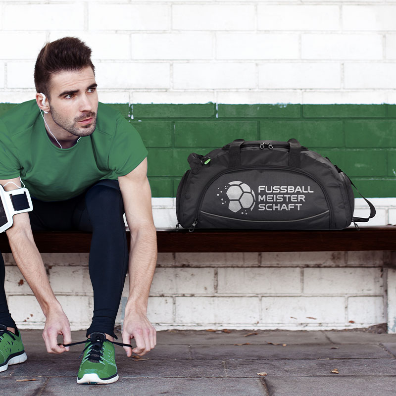 Ein Mann sitzt auf einer Bank und bindet sich die Sportschuhe. Neben ihm steht eine schwarze Sporttasche.