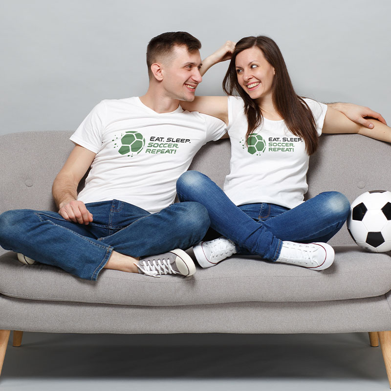 Ein Mann und eine Frau sitzen auf einem Sofa und tragen ein Fanartikel T-Shirt.