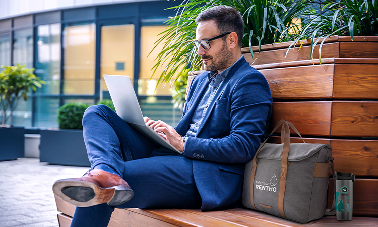 Ein Business-Mann sitzt mit Anzug, Laptop und Laptoptasche auf einer Bank Ein Business-Mann sitzt mit Anzug, Laptop und Laptoptasche auf einer Bank