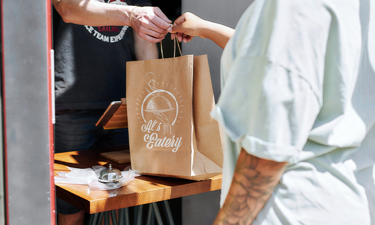 Ein Mitarbeiter gibt einem gast ein Papiersackerl mit Essen to-go