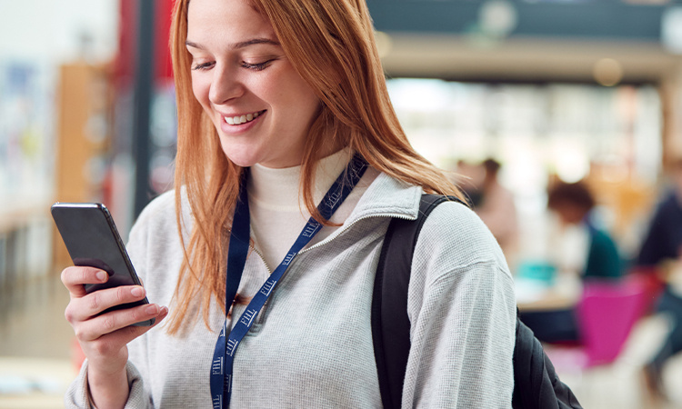 Junge Frau hält ein Handy in der Hand und trägt einen bedruckten Lanyard um den Hald