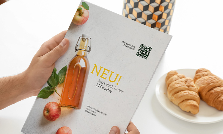 Produktkatalog versehen mit einem QR-Code, im Hintergrund ein Teller mit Croissants