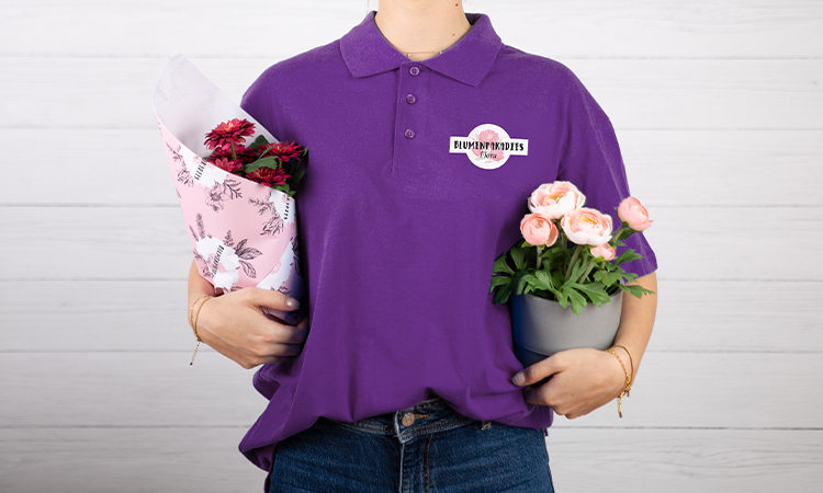 Frau mit bedrucktem Polo-Shirt hält Pflanzen in beiden Armen Frau mit bedrucktem Polo-Shirt hält Pflanzen in beiden Armen