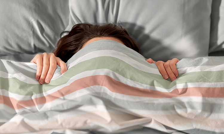 Frau versteckt sich unter der bedruckten Bettwäsche Frau versteckt sich unter der bedruckten Bettwäsche